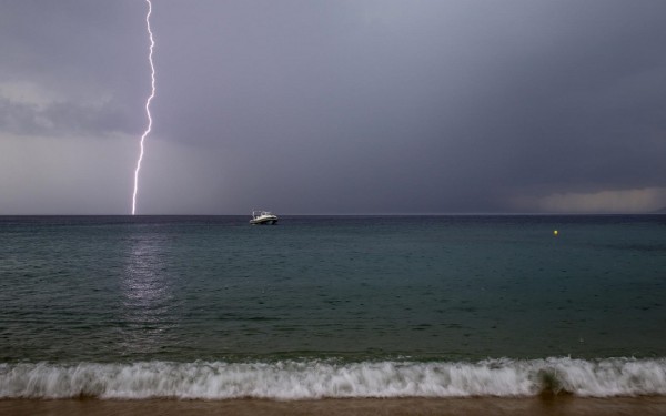Lightning strikes as a small boat is seen at the beach in the northern Greek village of Toroni