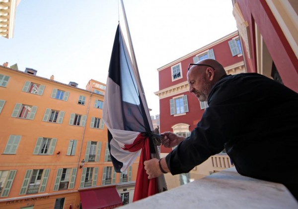 A municipal employee ties a black ribbon around the French flag in a sign of mourning to victims the day after a series of fatal shootings in Paris, at the city hall in Nice, France, Nobember 14, 2015. REUTERS/Eric Gaillard