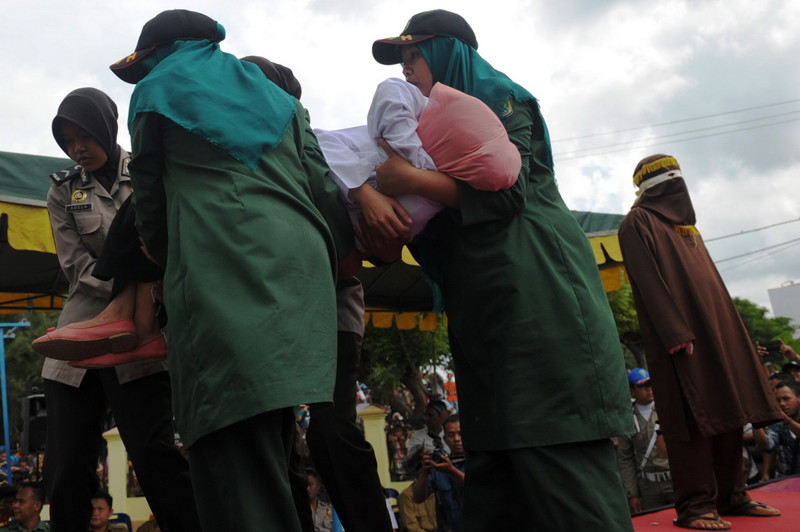 A young Acehnese woman is carried by officials after being caned in public, a punishment under the Islamic sharia law, under the offence of "khalwat" or "close proximity" between a man and a woman who are not spouses, in Banda Aceh on December 28, 2015. Aceh is the only province of Indonesia enforcing the Islamic Sharia law and offenders are punished by public caning. / AFP / CHAIDEER MAHYUDDIN