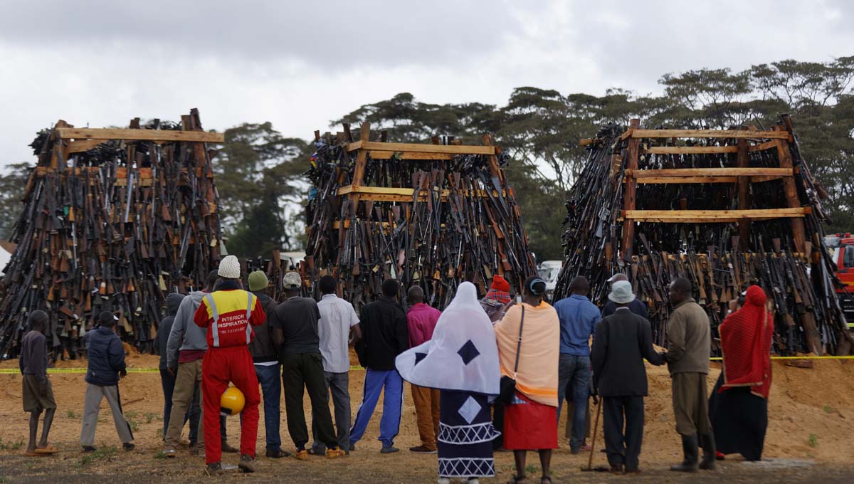 People watch before a pile of 5,250 illegal weapons are burned by Kenyan police in Ngong, near Nairobi, in Kenya Tuesday, Nov. 15, 2016. The weapons consisted of both confiscated and surrendered firearms that had been stockpiled over almost a decade and were destroyed by police as a message to the public to surrender others. (AP Photo/Ben Curtis)