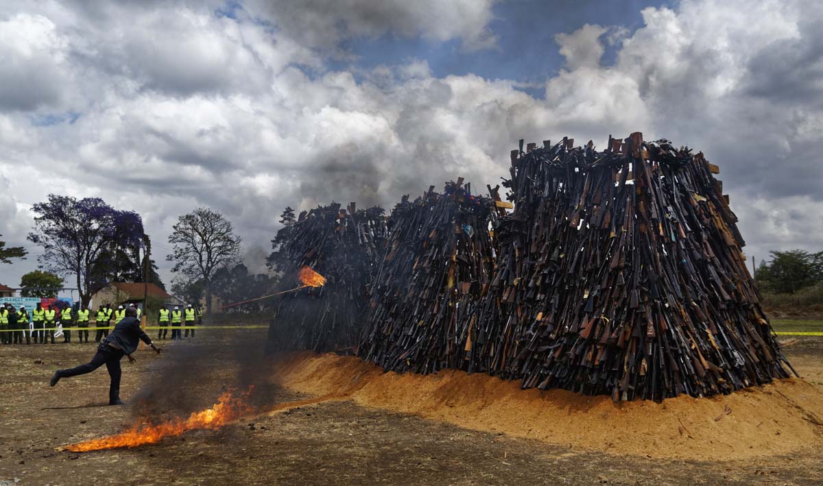 A man throws a torch to set light to a pile of 5,250 illegal weapons as they are burned by Kenyan police in Ngong, near Nairobi, in Kenya Tuesday, Nov. 15, 2016. The weapons consisted of both confiscated and surrendered firearms that had been stockpiled over almost a decade and were destroyed by police as a message to the public to surrender others. (AP Photo/Ben Curtis)