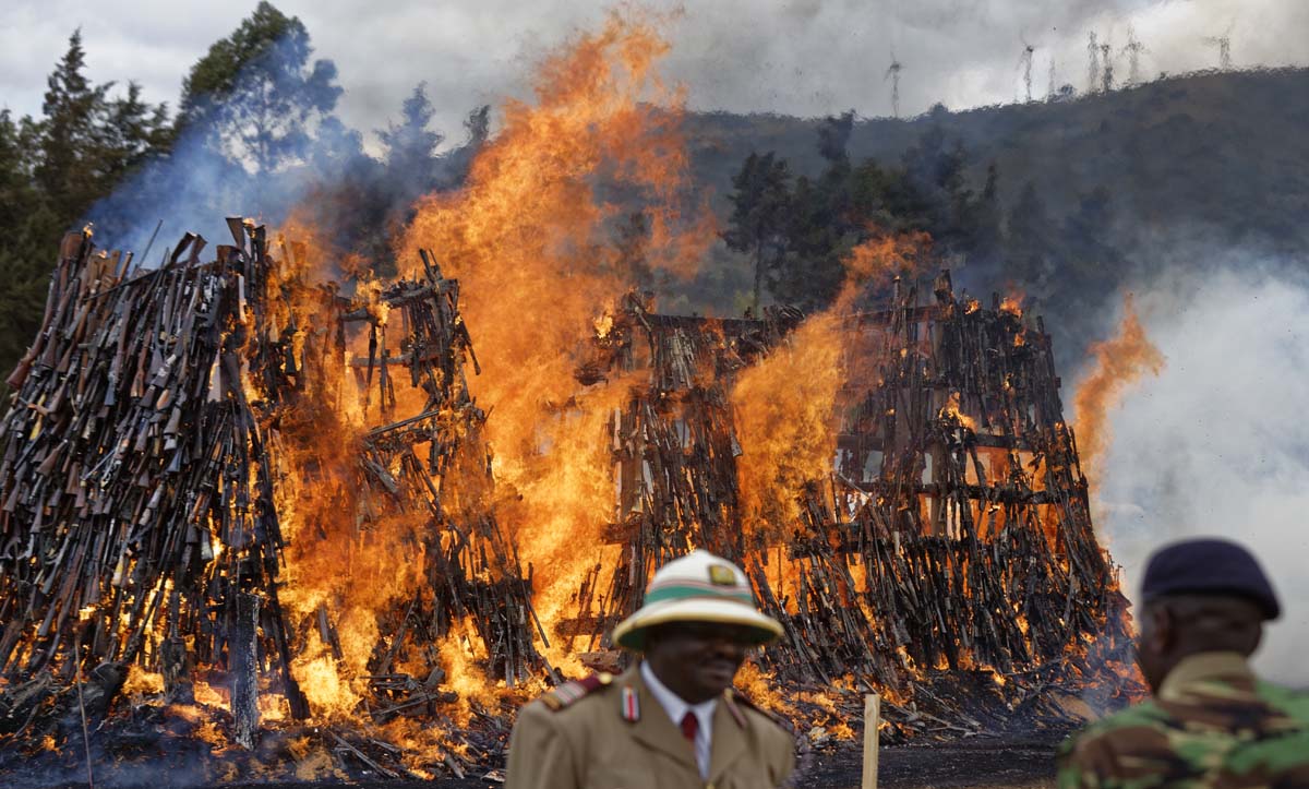 Kenyan police and officials watch as a pile of 5,250 illegal weapons are burned by Kenyan police in Ngong, near Nairobi, in Kenya Tuesday, Nov. 15, 2016. The weapons consisted of both confiscated and surrendered firearms that had been stockpiled over almost a decade and were destroyed by police as a message to the public to surrender others. (AP Photo/Ben Curtis)